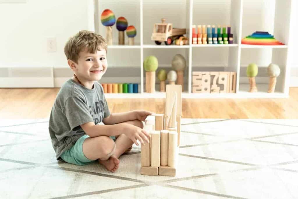 A boy plays with wooden blocks on a carpet building a castle. 