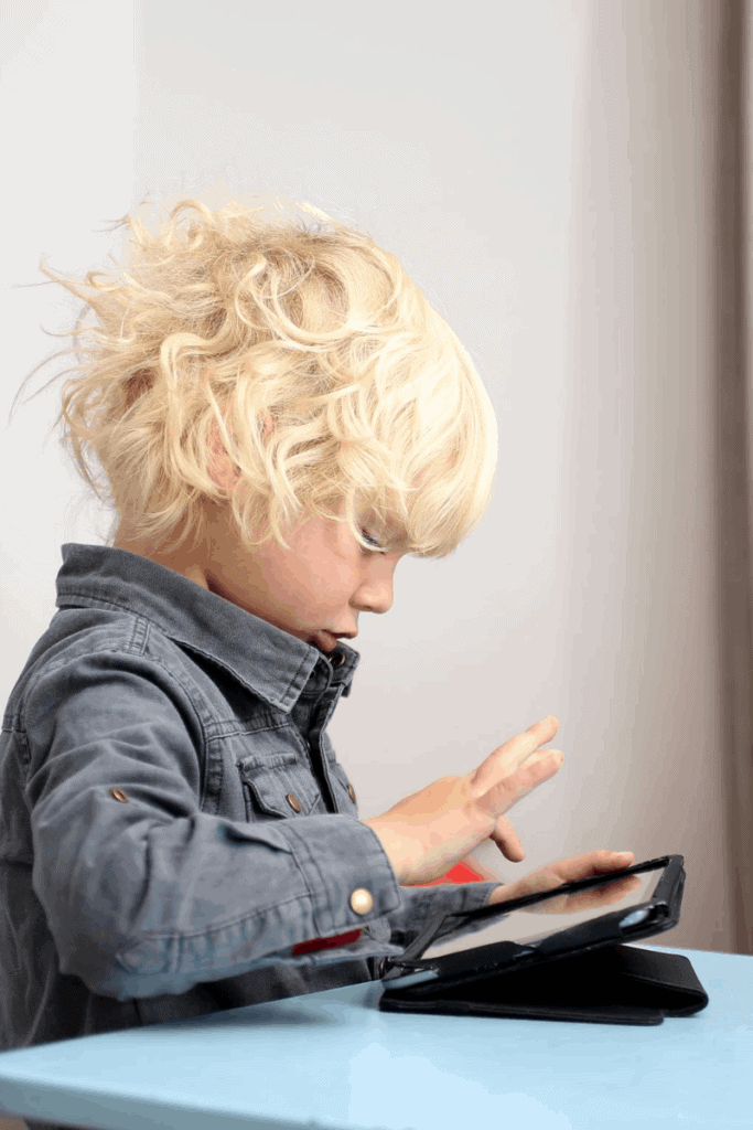 A boy playing on a tablet sitting on a blue table.