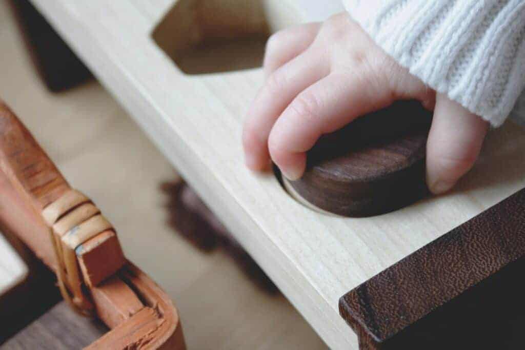 Toddler hand playing with a shape sorter puzzle one of the many Montessori toy options out there. 