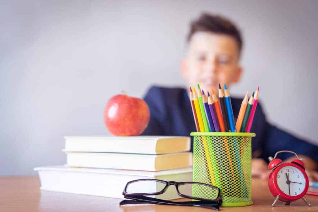 A child sitting behind a desk out of focus with pencils and books all in a row lined up and organized. 