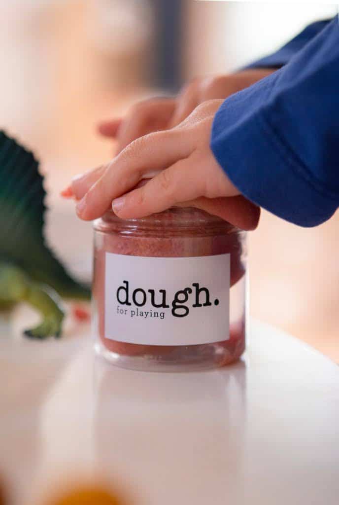 A child's hand pushing red play dough back into a jar