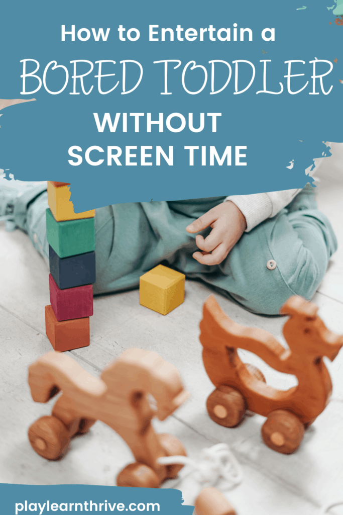 A child sits on a wooden floor playing with wooden stacking blocks and wooden toys with wheels over coming toddler boredom.