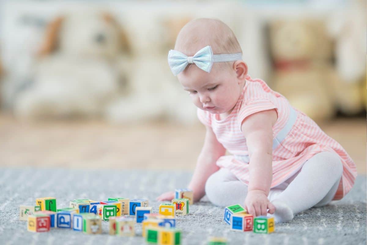 a baby sits on a rug playing with blocks as a part of a pincer grasp activity