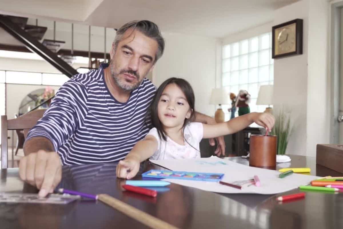 dad and daughter sit at a table together going over homework and practicing life skills that the child will need to develop in life