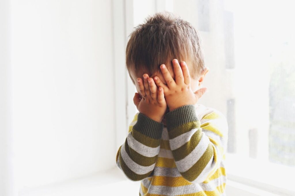 Toddler covers his face with his hands because he is upset.