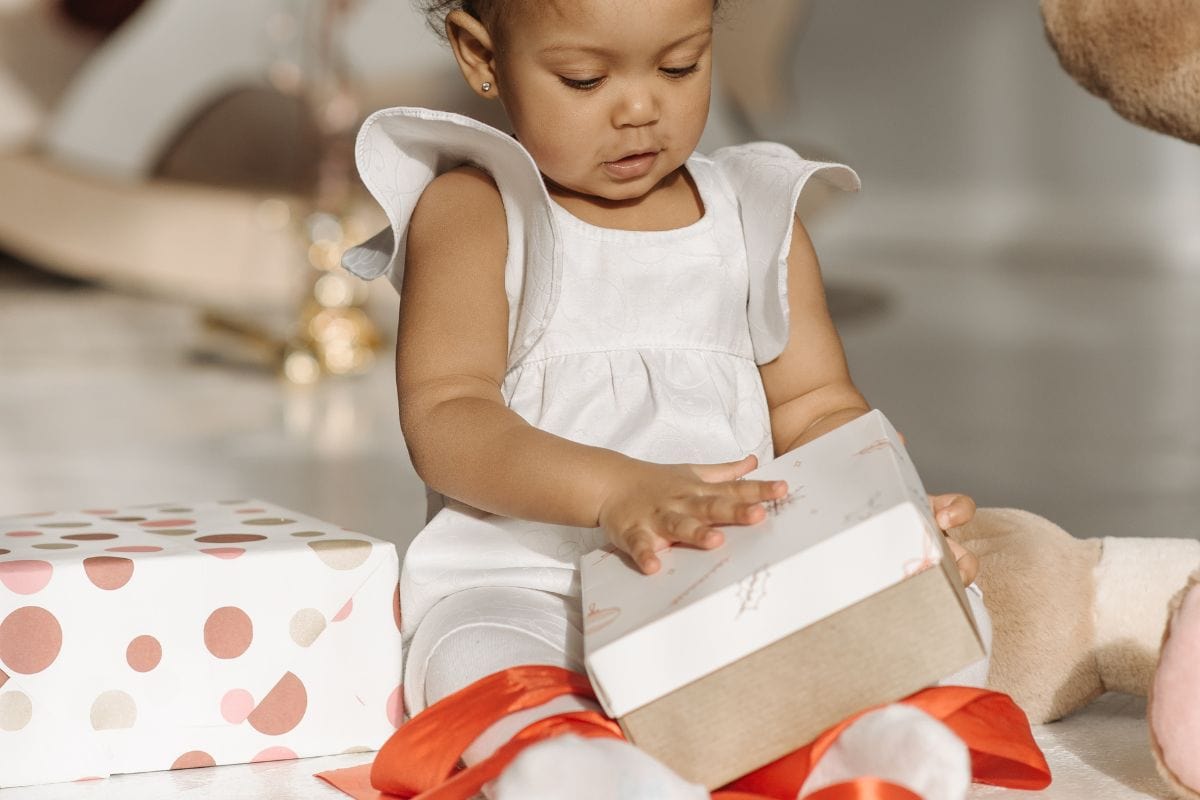 brown skinned baby opening a white gift box with red ribbon