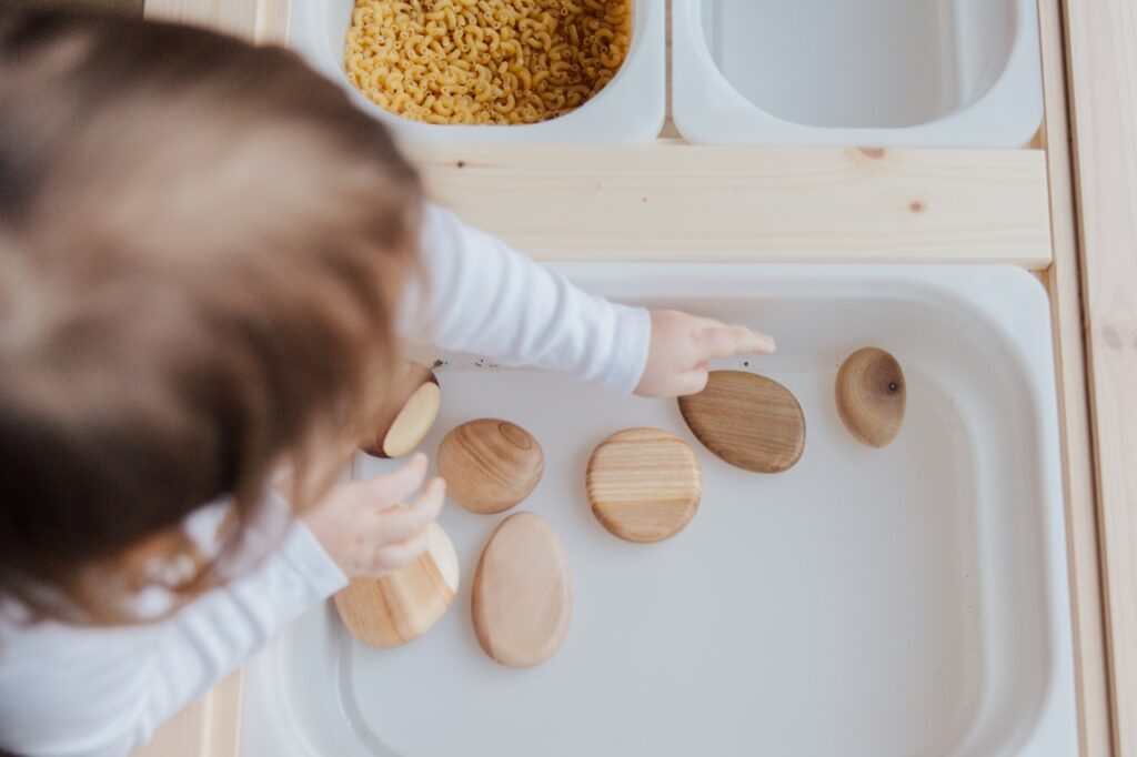 small child using wooden rocks in a sensory play tray